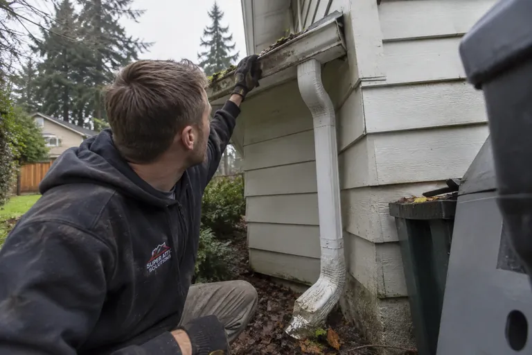 A technician checking an overflowing gutter and a downspout that ends at the foundation